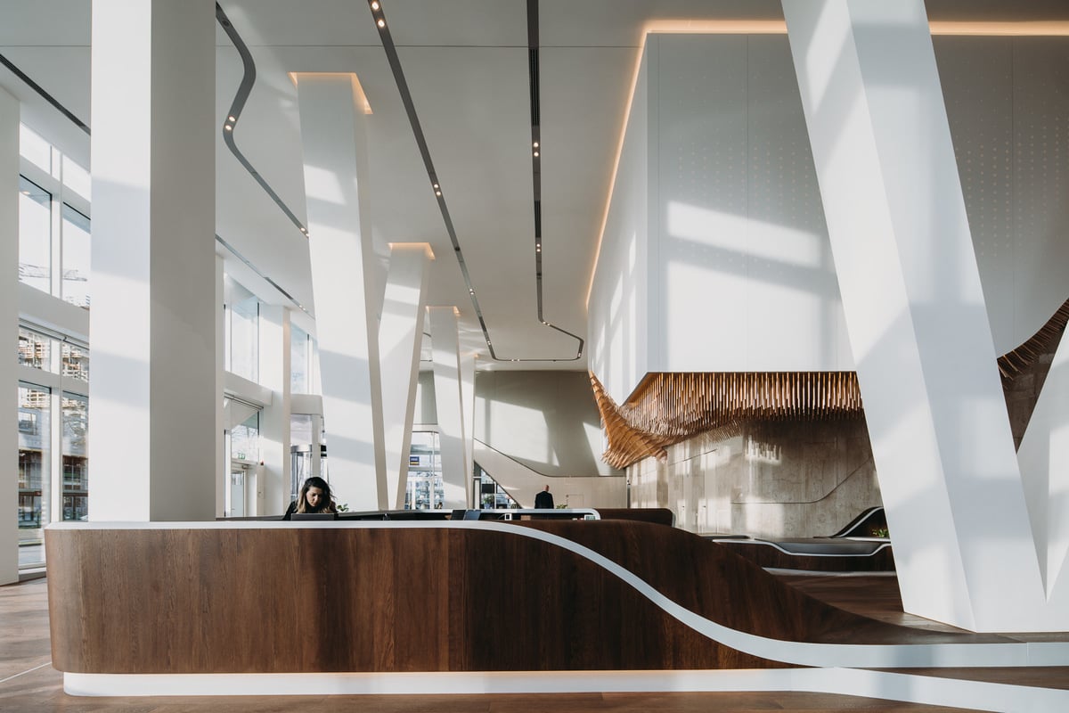 Grootschalig naadloos akoestisch plafond in een hoge, moderne kantoorlobby met veel glas en natuurlijke lichtinval, gerealiseerd door Pennings.
