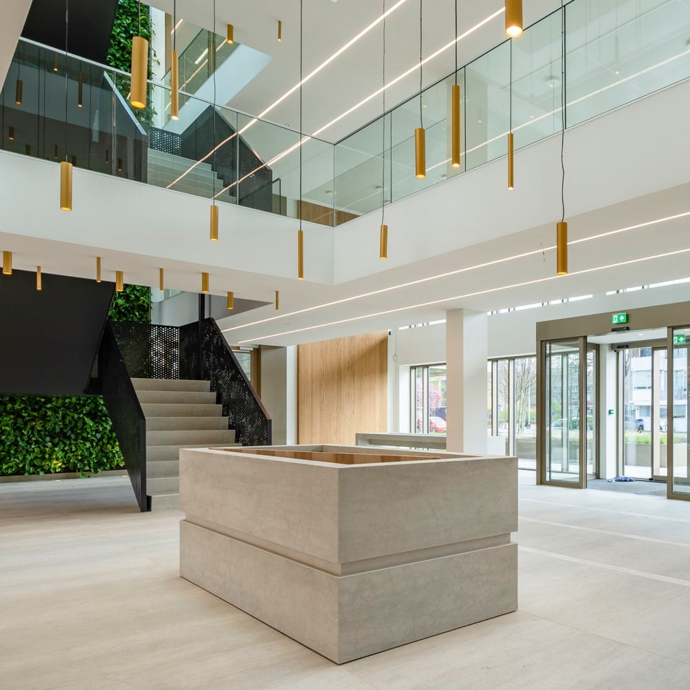 Modern kantoorinterieur met een naadloos wit akoestisch plafond van Pennings in een hoge open vide en receptieruimte, ontworpen voor optimale geluidsabsorptie en spraakverstaanbaarheid.